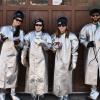 Four women standing in front of a garage wearing aluminum-rayon coats, spats, and kevlar gloves that give a sci-fi aesthetic 