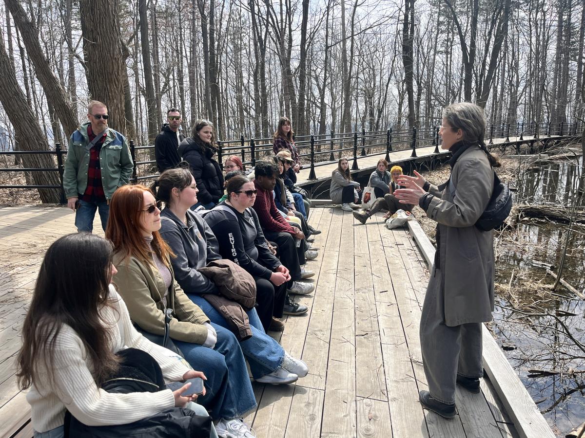 Katherine Davies standing in front of seated students on a wetland boardwalk