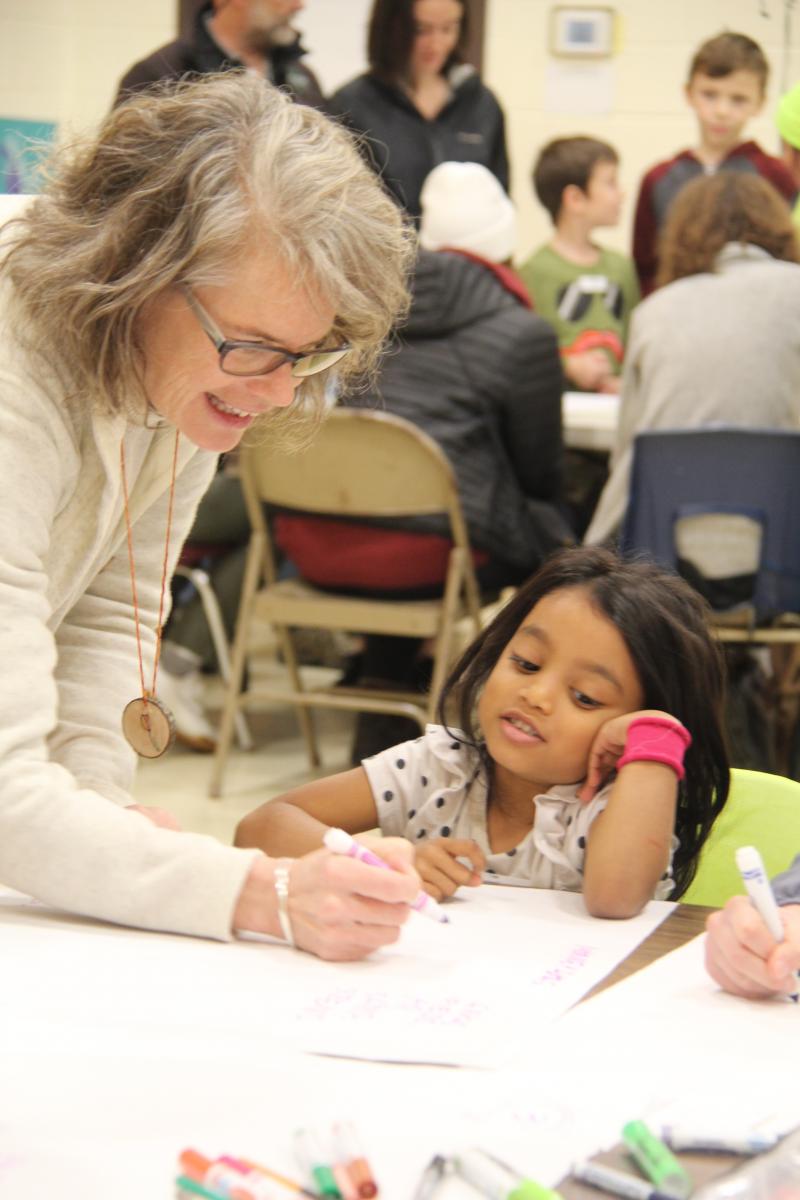 Student drawing at table with student looking