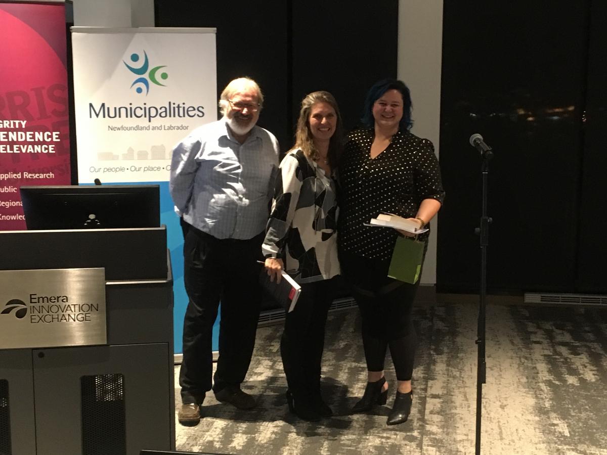 Three people in front of conference poster and podium