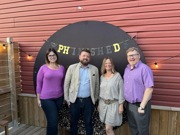 Four people standing in front of round sign outside