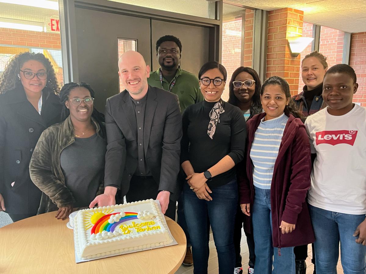 Dr. Tarhan holding a cake and gathered around by graduate students