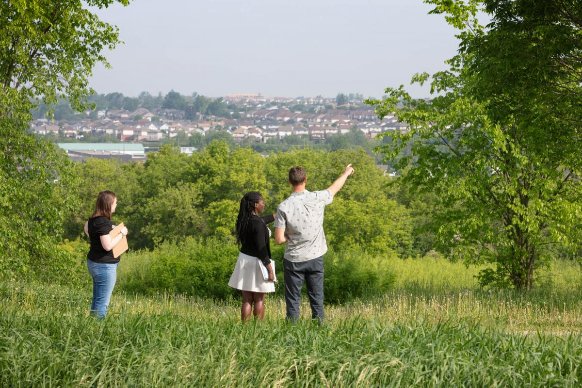 Three people standing in open field looking at subdivision of houses