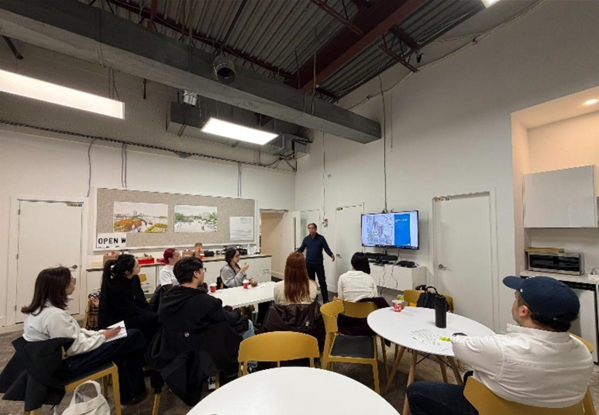 Students sitting at tables listening to speaker at the front of the room