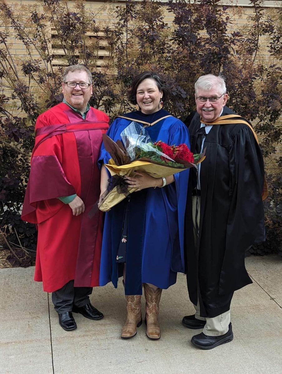 Dr. Weeden holding flowers and standing beside Dr. Ryan Gibson and James Weeden