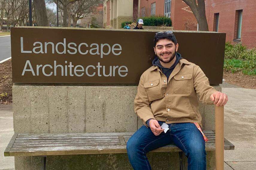 David DeBono sitting on bench in front of landscape architecture building sign