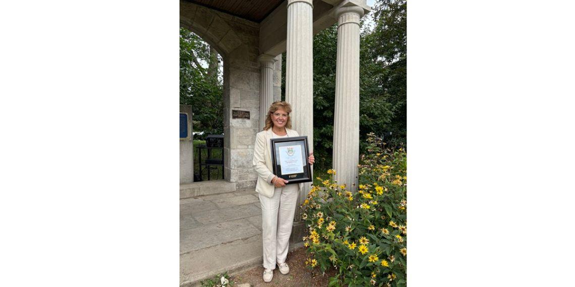 Person holding framed award standing in front of portico