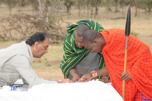 People gathering around table viewing drawings with field in background