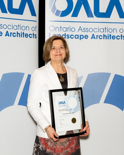 Cecelia Paine holding certificate behind OALA banners