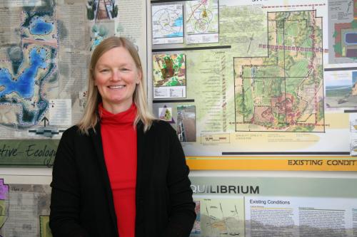 Photo of Karen Landman in front of design drawings and maps