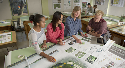 Students standing at drafting table receiving advice on landscape drawings