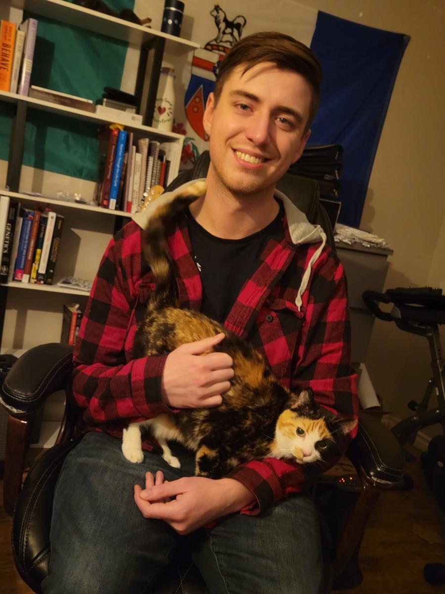 Photo of Myles St Denis wearing a red and black plaid shirt holding a cat