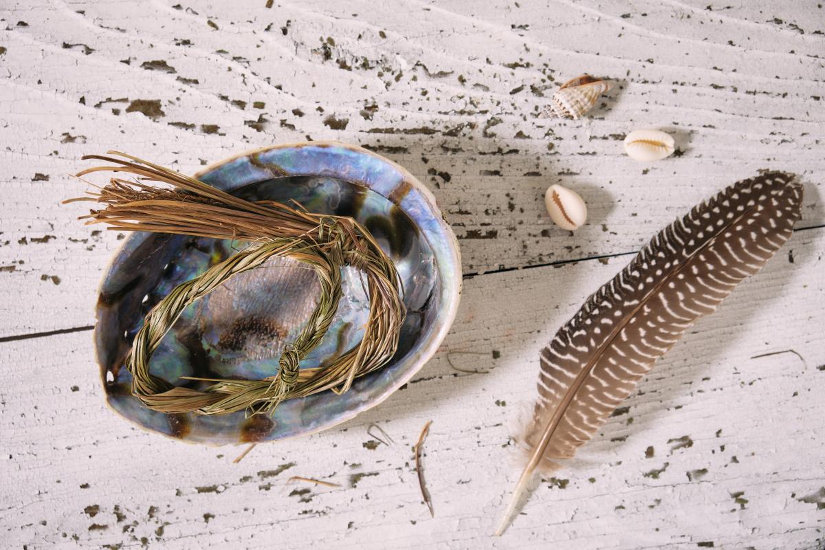 Braided sweetgrass in an abalone shell next to a turkey feather.
